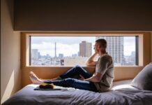 뇌건강, 지금부터 챙겨야 할 이유와 실천법 Man relaxes on a bed, gazing at a city view.