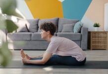 만성피로, 바쁜 일상 속 에너지 되찾는 ‘소소한 실천’이 해법 Woman stretching on yoga mat in living room.