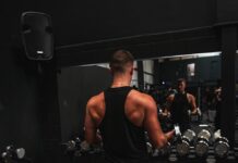 티셔츠 한 장으로 완성되는 ‘직각 어깨’의 비밀: 프레임을 바꾸는 필라테스 a man standing in front of a mirror in a gym