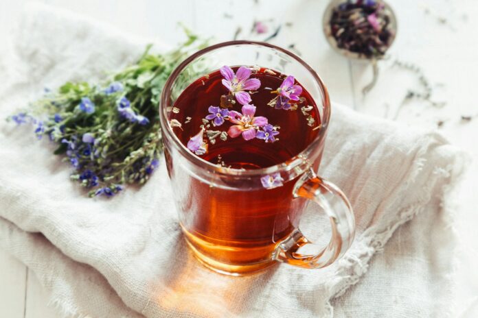 Photo by Elena Leya a glass mug filled with tea next to a bunch of flowers